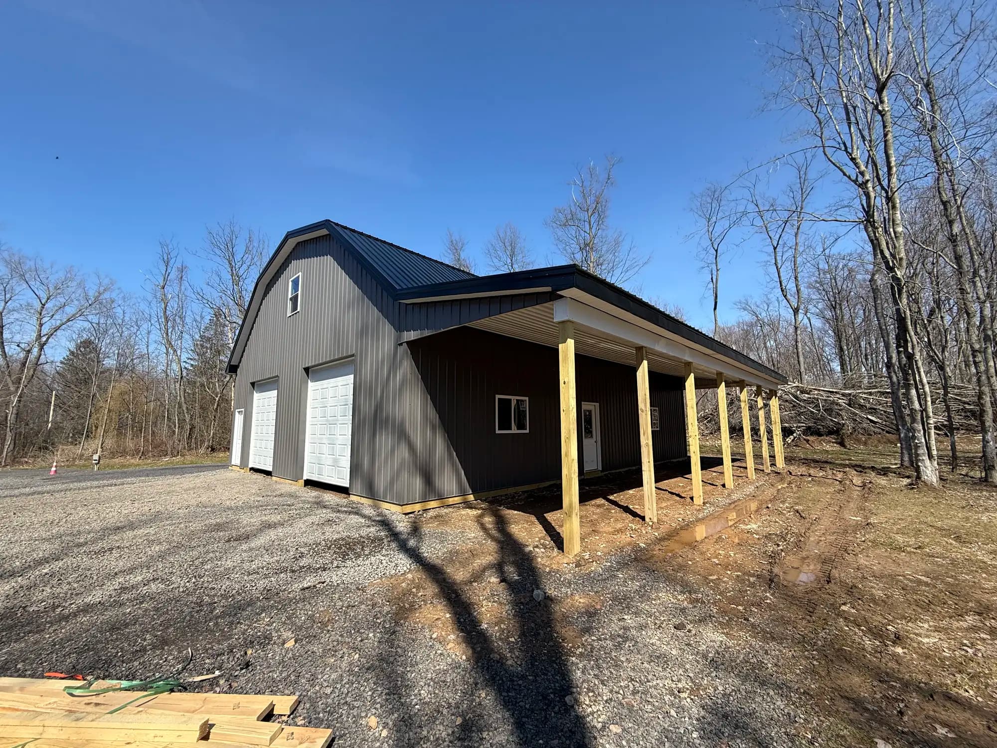 Barndominium with covered front porch, gambrel roof, and two garage doors
