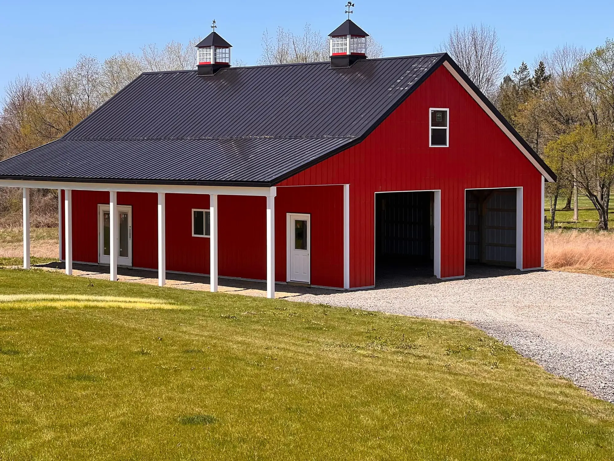 Red pole barn with covered porch, cupolas, and black metal roof
